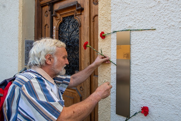 Ein Gast steckt Blumen an das Erinnerungszeichen für Hans Beimler